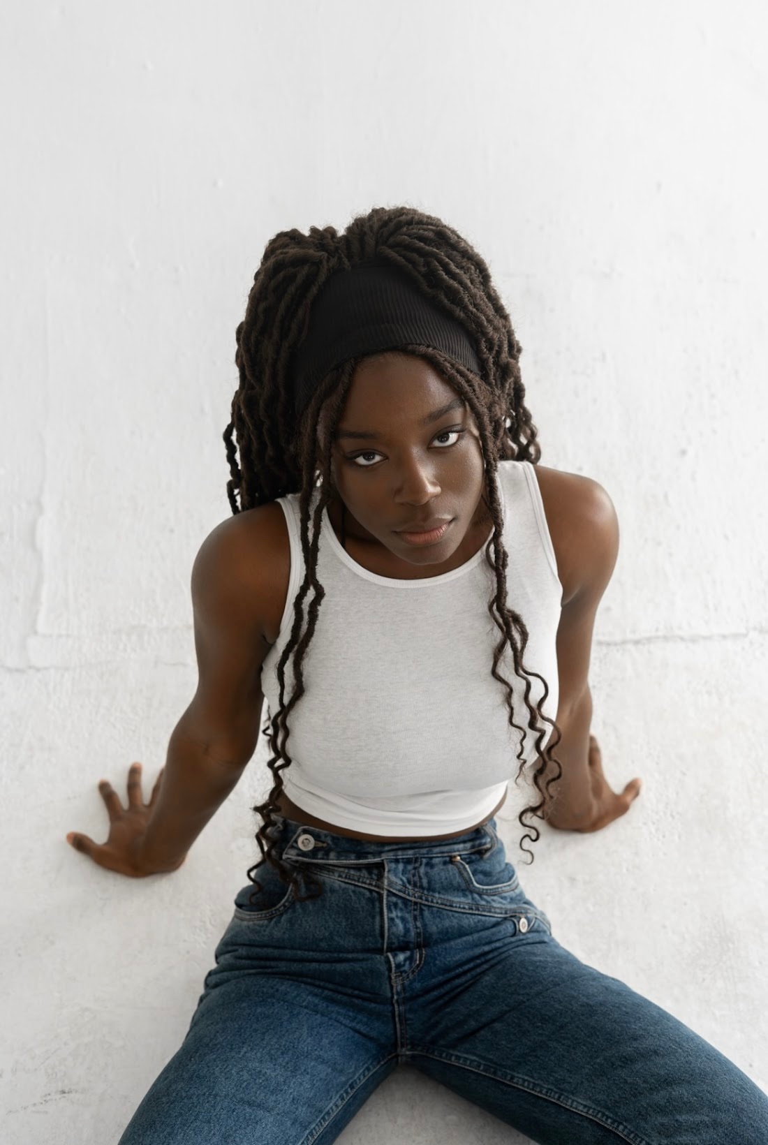 Noa Omane seated against white wall with braids